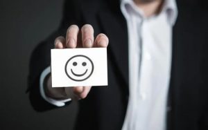 Uomo elegante che mostra un biglietto con disegnato uno smile felice