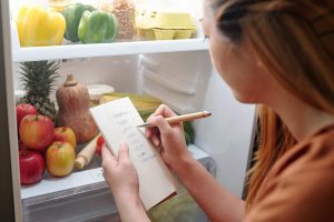Ragazza che fa la lista della spesa davanti al frigo