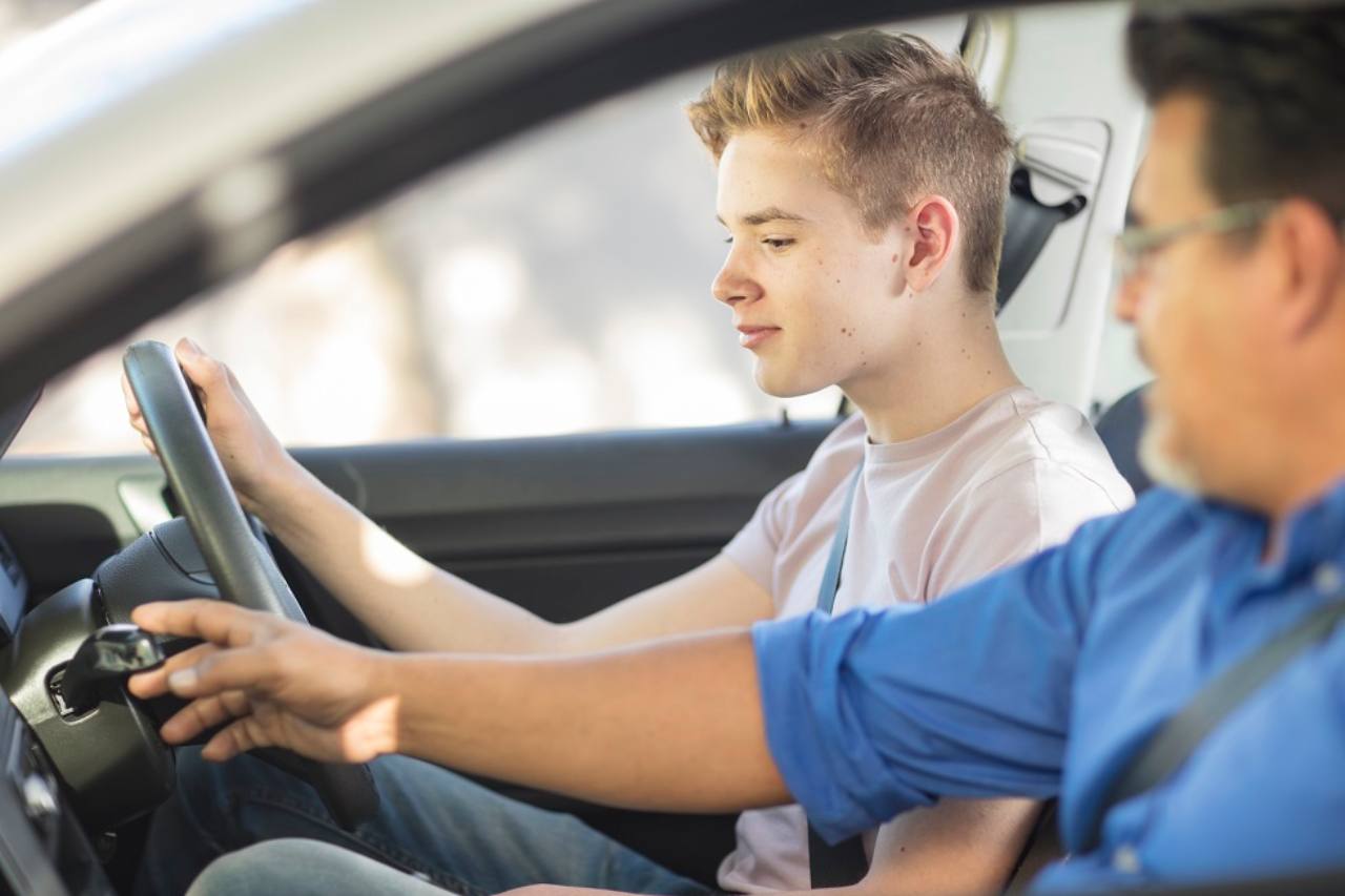 Adolescente che impara a guidare l'auto con l'aiuto di un adulto