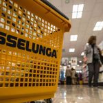 Carrello esselunga primo piano, scaffale e cliente sullo sfondo