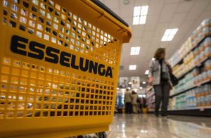 Carrello esselunga primo piano, scaffale e cliente sullo sfondo