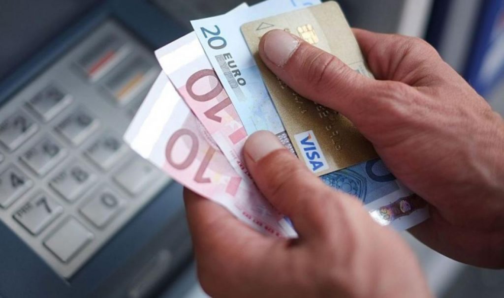 Uomo vicino al bancomat con in mano carta di credito e contanti