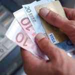 Uomo vicino al bancomat con in mano carta di credito e contanti