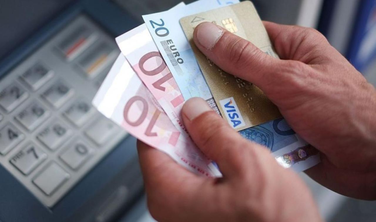 Uomo vicino al bancomat con in mano carta di credito e contanti