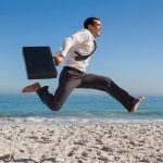 Lavoratore in camicia e cravatta che salta felice in spiaggia: ferie estive