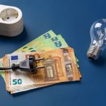 Banconote da 50 e 100€ sul tavolo, una spina della corrente, una lampadina e una ciabatta: spesa della luce