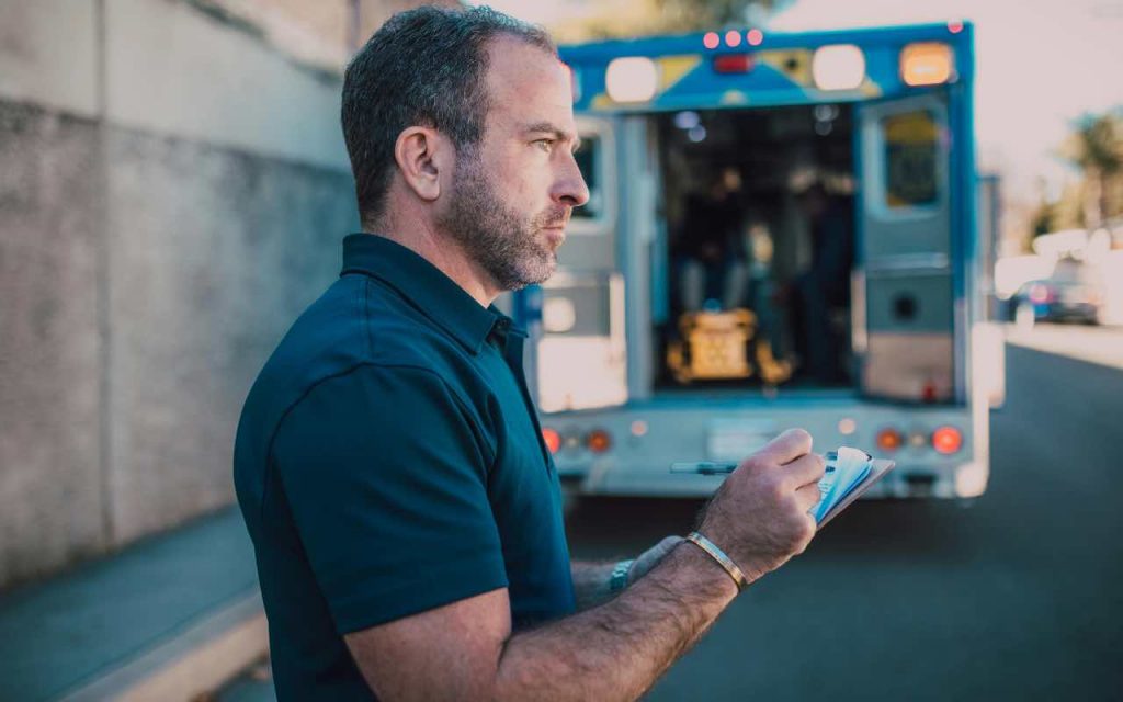 uomo che prende i rilevamenti con alle spalle un’ambulanza