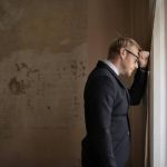 uomo disperato con la testa appoggiata al muro